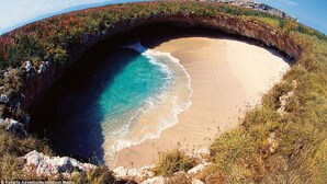 Ein natürlicher Felsbogen über einem Strand mit klarem türkisblauem Wasser.