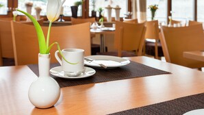 Een eettafel met een witte vaas met een tulpenbloem, een witte kop en een schotel.