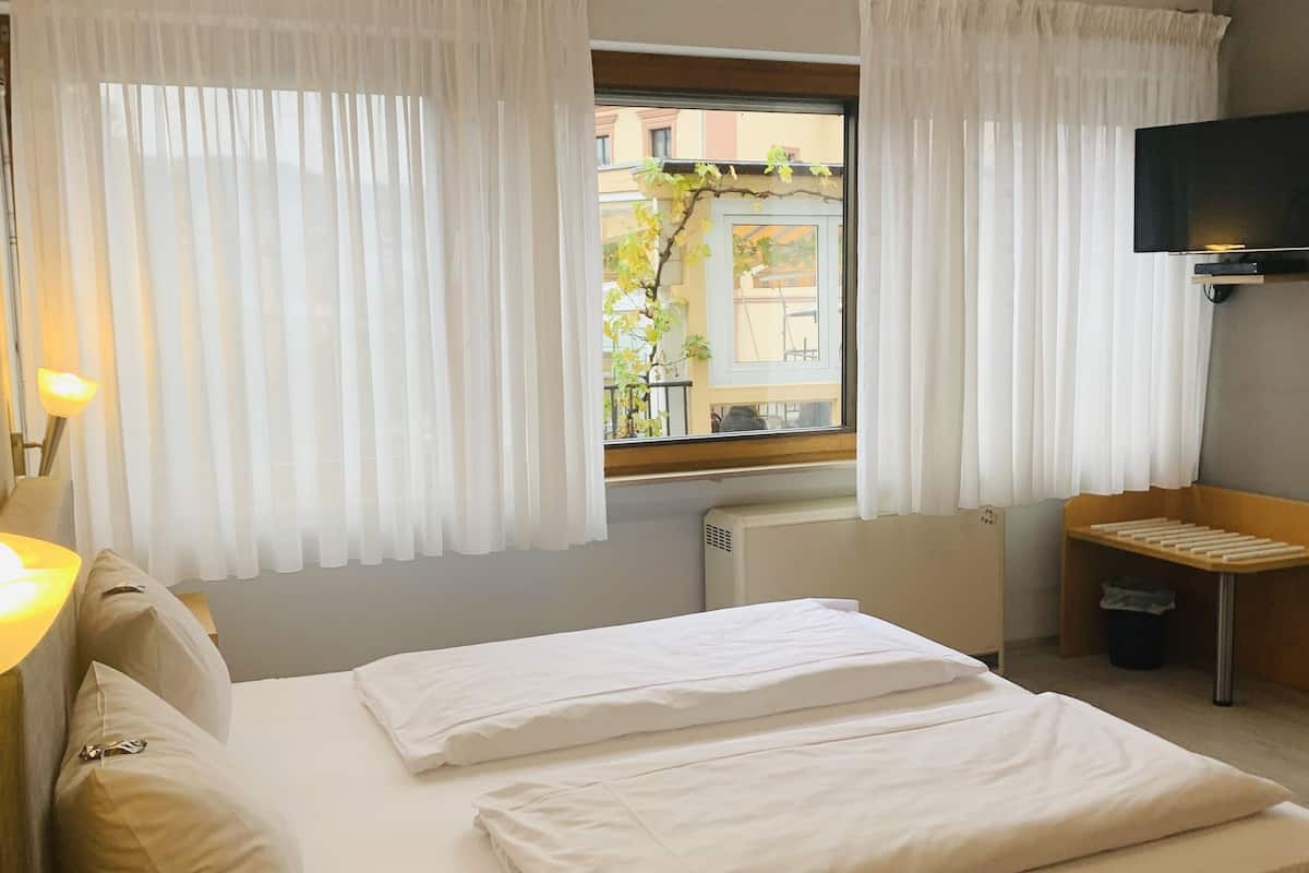 A hotel room with a bed, a desk, a chair, a TV, and a window with curtains.