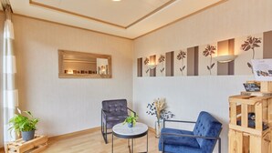 Een moderne kamer met een houten vloer, een ronde tafel met een bloempot, een blauwe fauteuil, een grijze leren stoel en een houten bijzettafeltje met een bloevas.