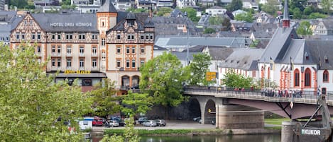 A historic building with a prominent tower and multiple windows, located near a river with a bridge crossing over it.
