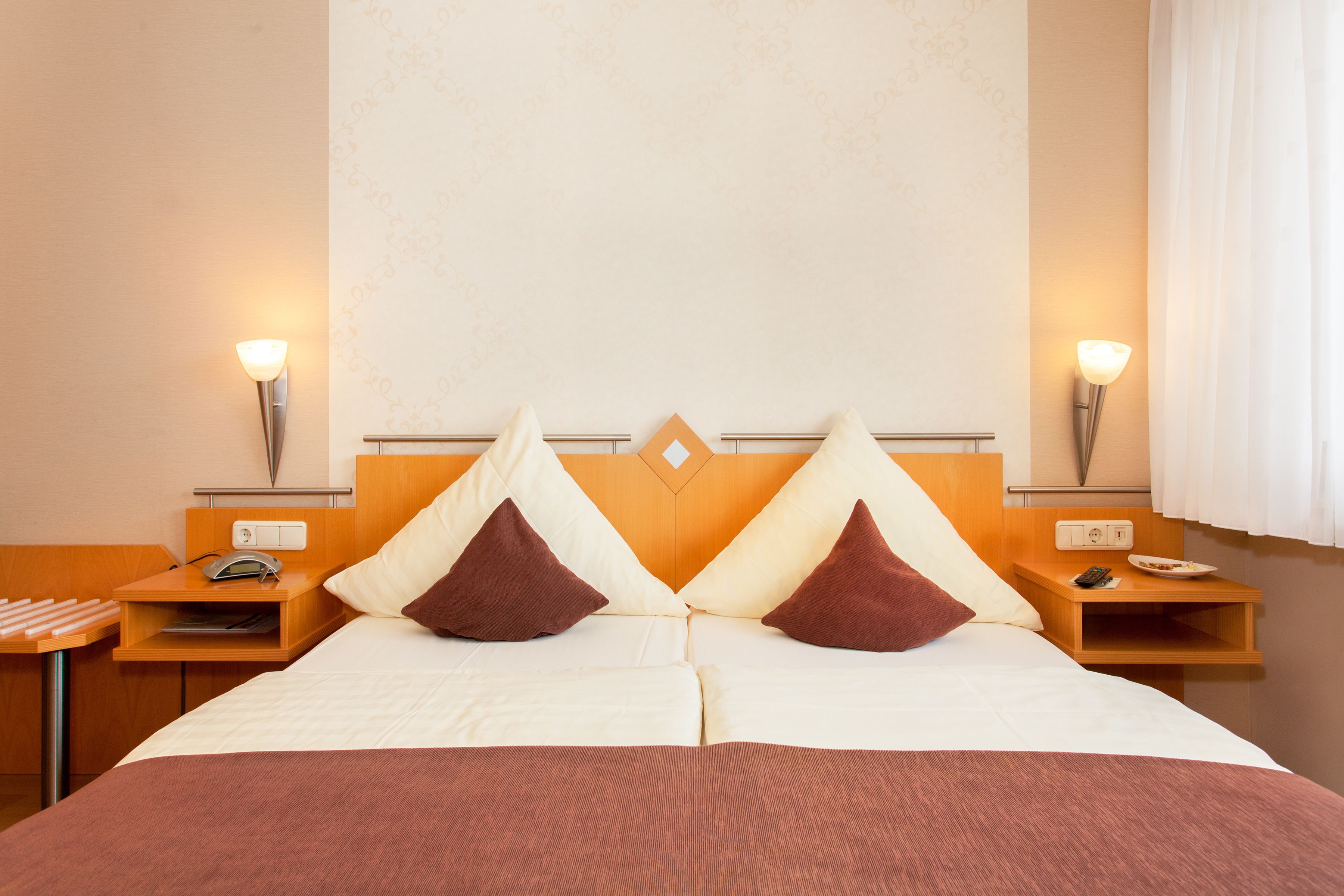 A double bed with two pillows, a bedside table with a lamp, and a nightstand with a phone and a bowl.