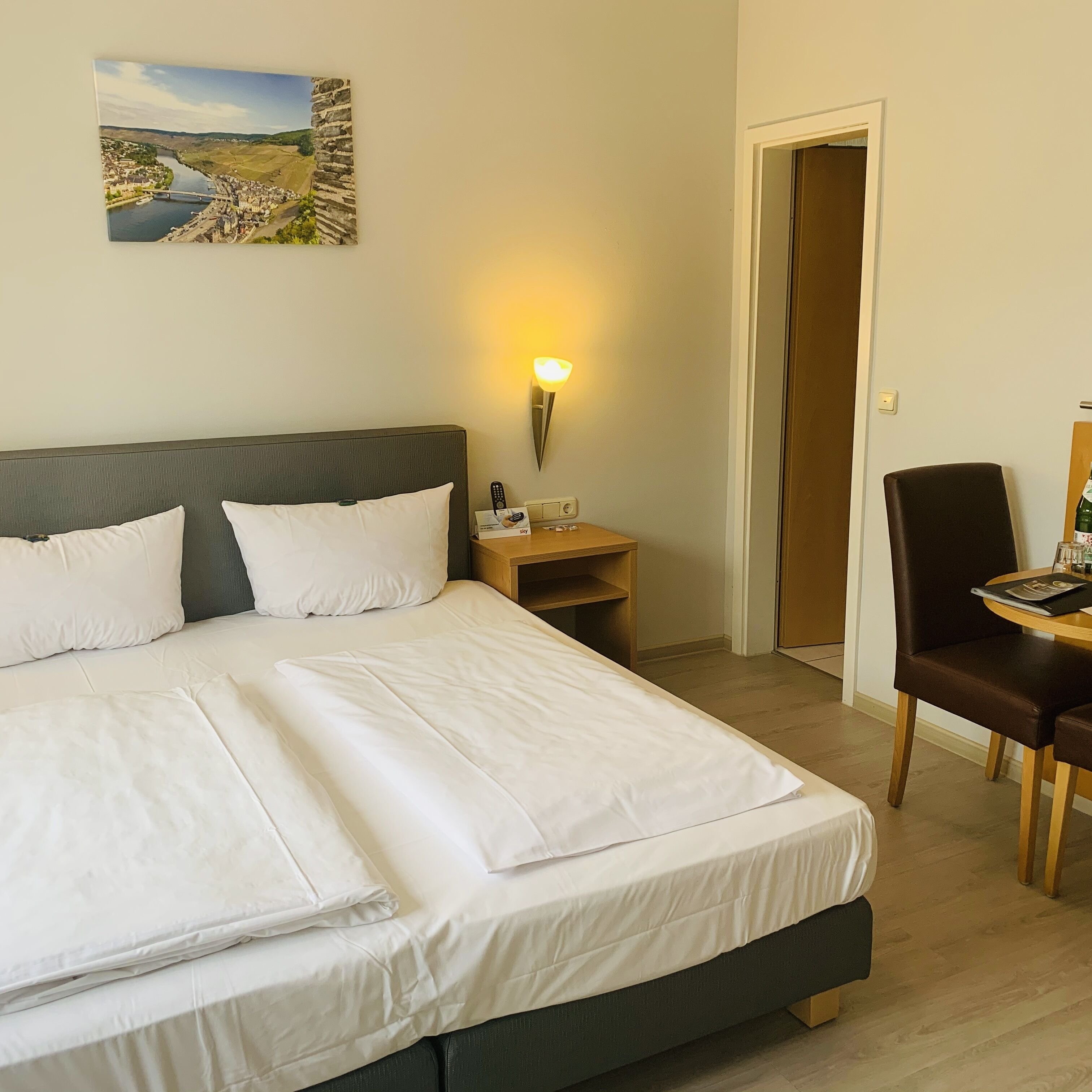 A neatly made bed with white linens, a bedside table with a lamp, and a chair with a table.