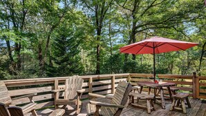 A wooden deck with Adirondack chairs, a picnic table, and a red umbrella.