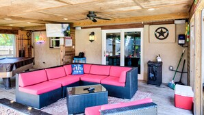 A covered outdoor area with a pool table, a red sectional sofa, and a ceiling fan.