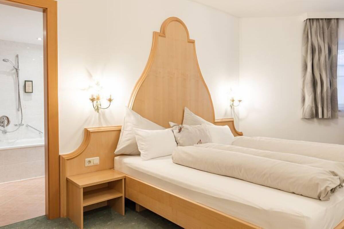 A hotel room with a wooden bed, bedside lamps, a nightstand, and a shower area.