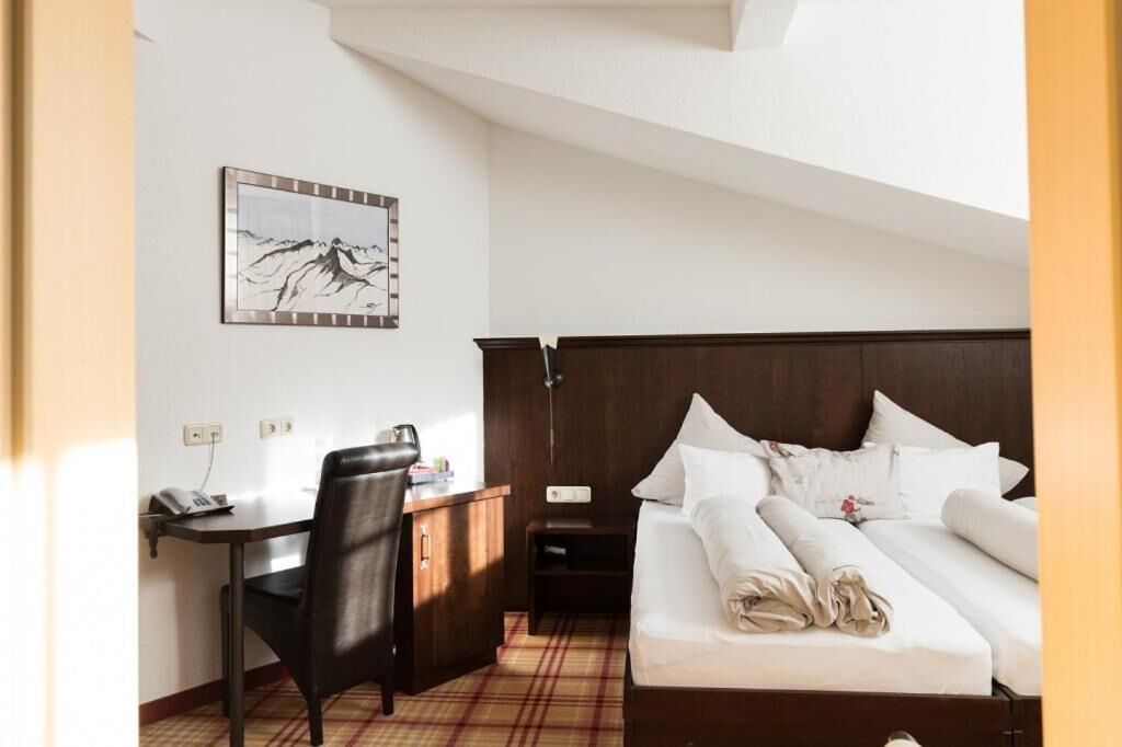 Habitación de hotel con cama, escritorio, silla, mesita de noche, lámpara y una obra de arte colgada en la pared.