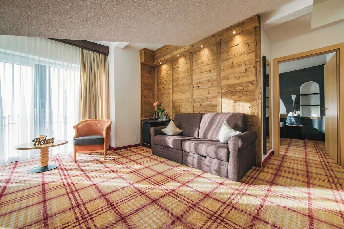 A cozy living room with a plaid carpet, a sofa, a chair, and a small table with a 'Relax' sign.
