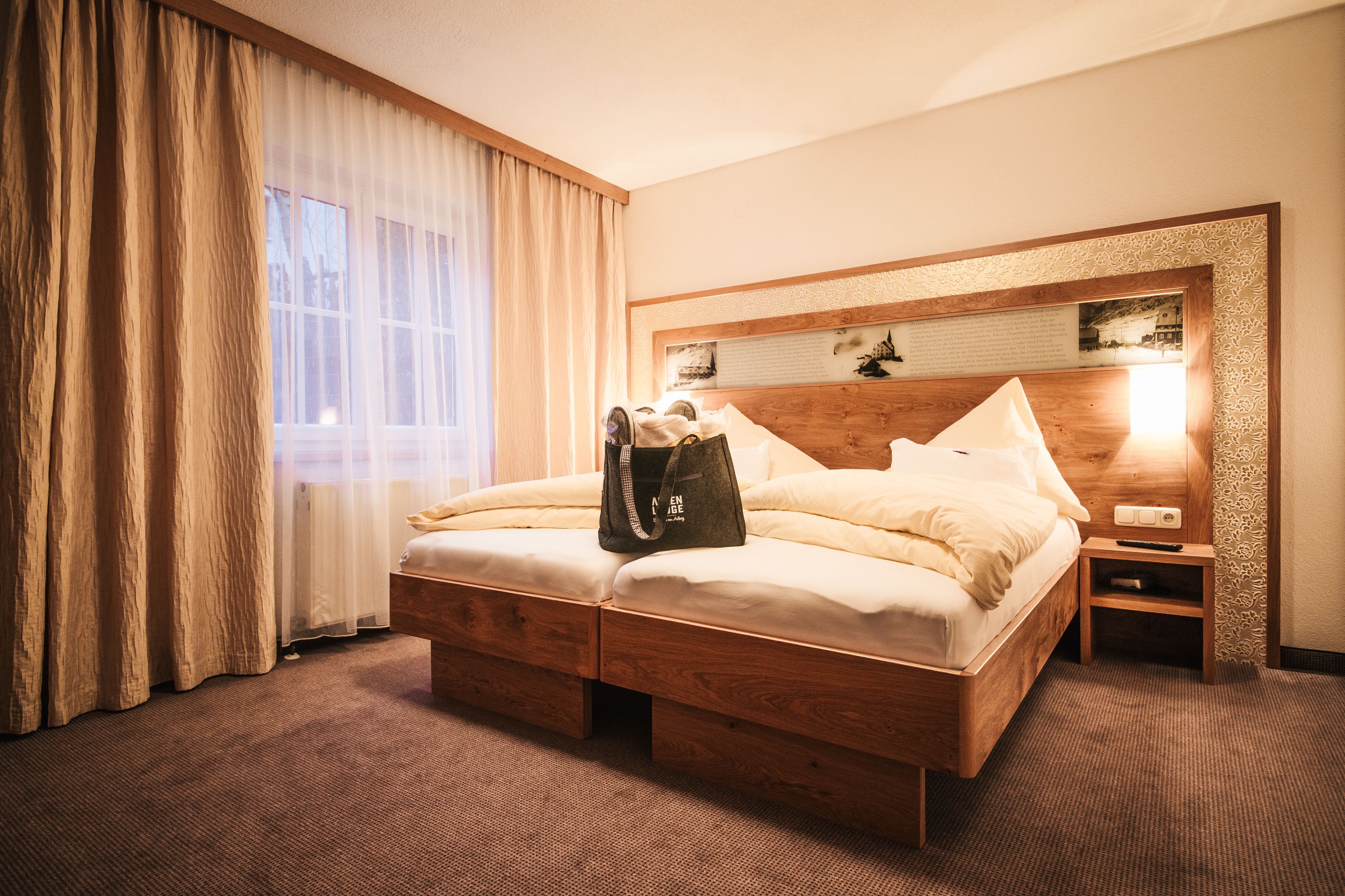 A hotel room with a wooden bed, a nightstand, a lamp, and a window with curtains.