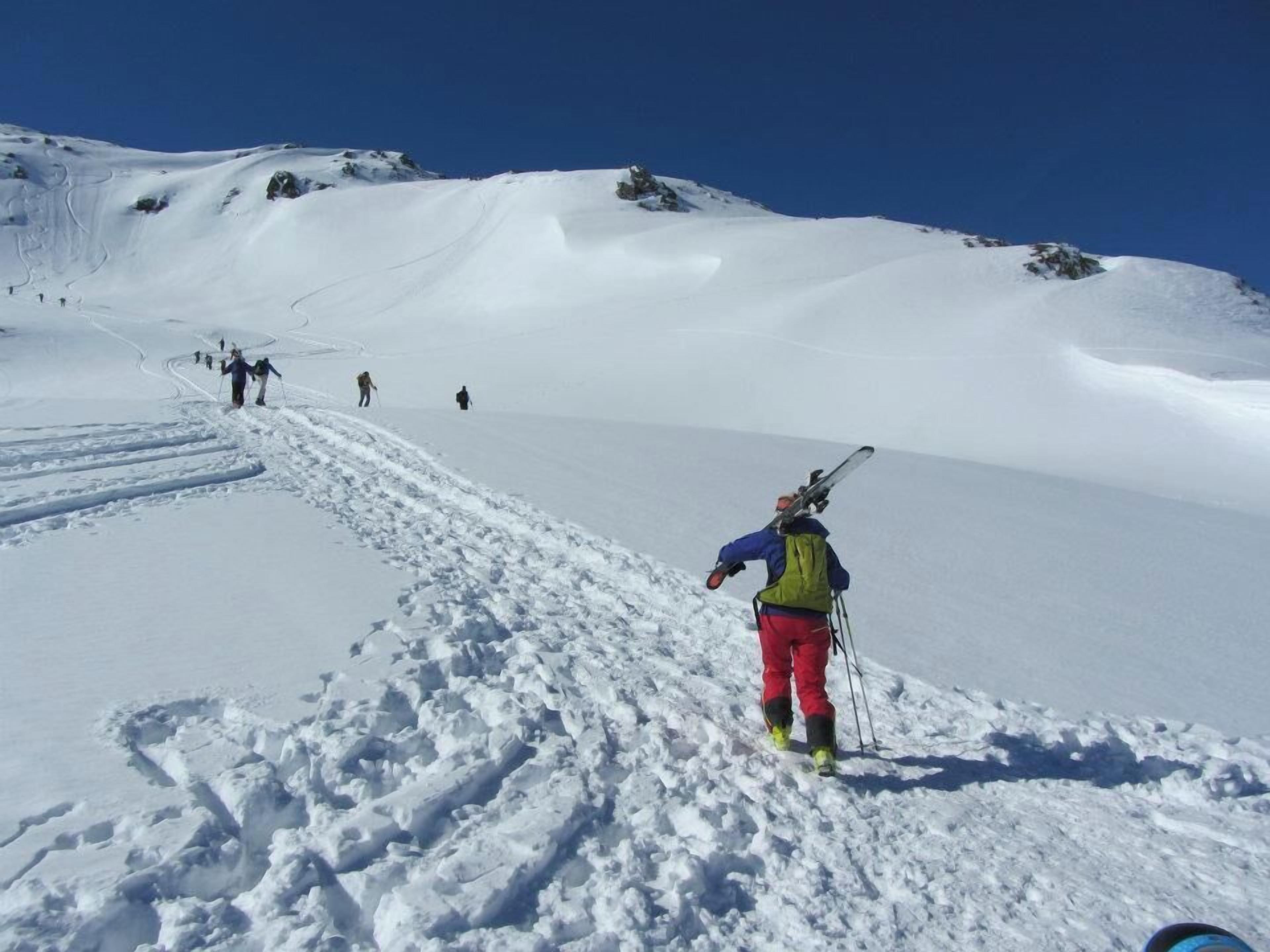 Un sendero nevado en la montaña con esquiadores ascendiendo.