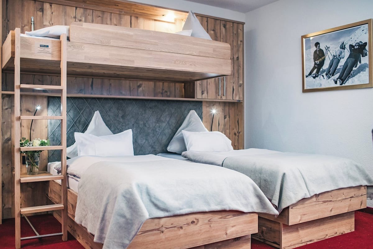 A bunk bed room with a wooden ladder, two beds, a shelf with a plant, and a framed picture on the wall.