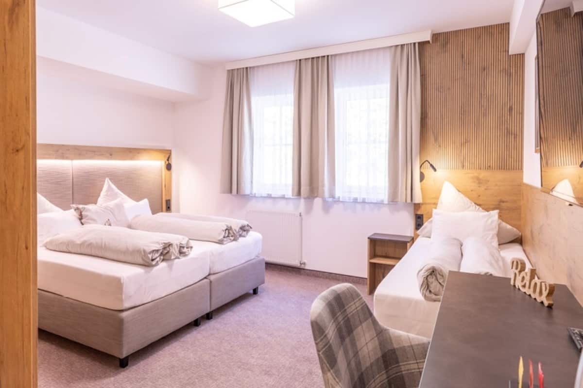 A hotel room with a bed, a desk, a chair, and a large window with curtains.