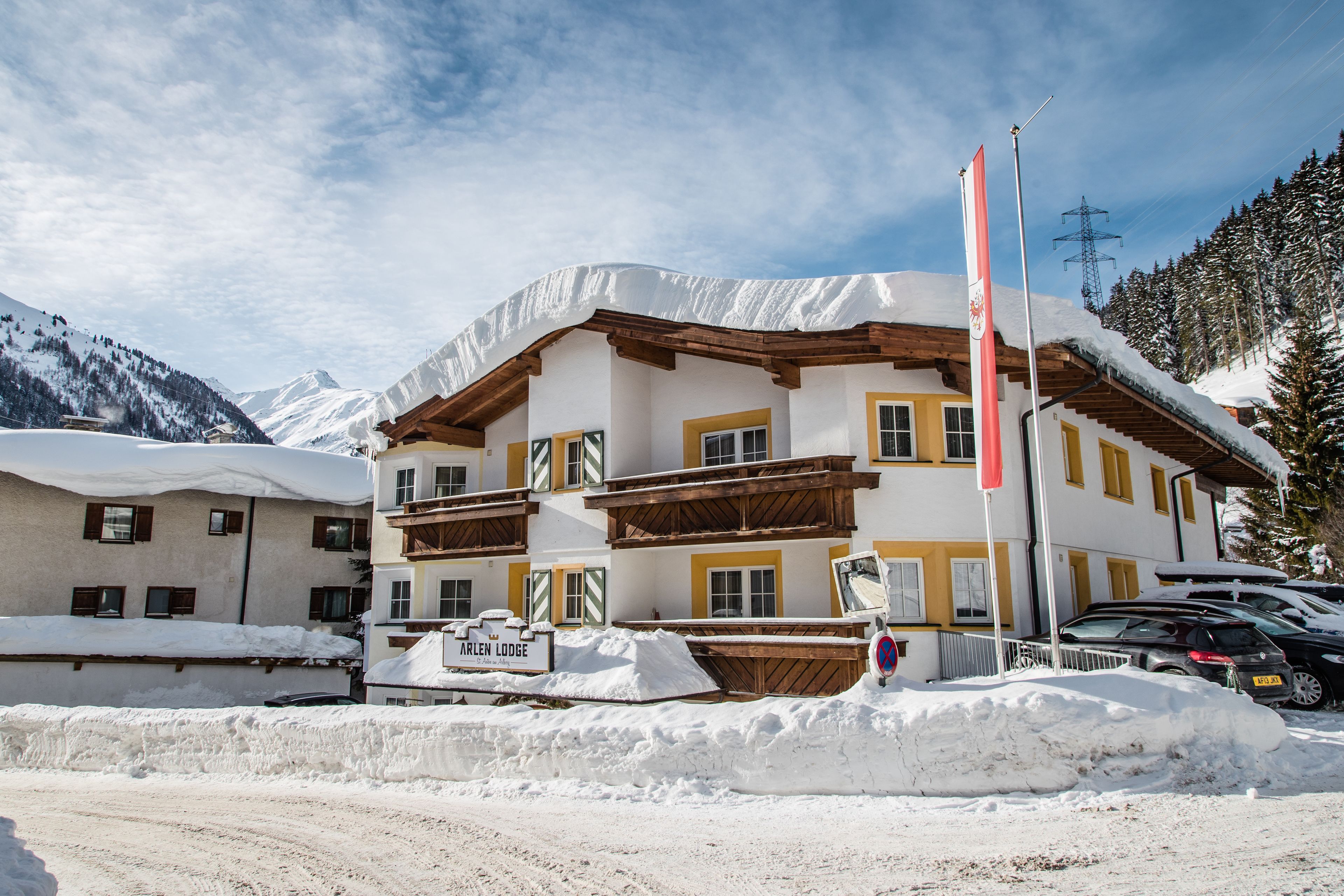 Un immeuble à plusieurs étages, dont le toit et les balcons sont recouverts de neige, entouré de neige et de montagnes.