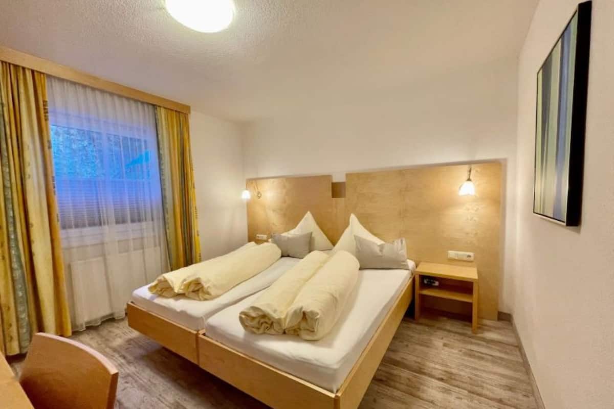 A hotel room with a double bed, bedside tables, a desk, and a window with curtains.