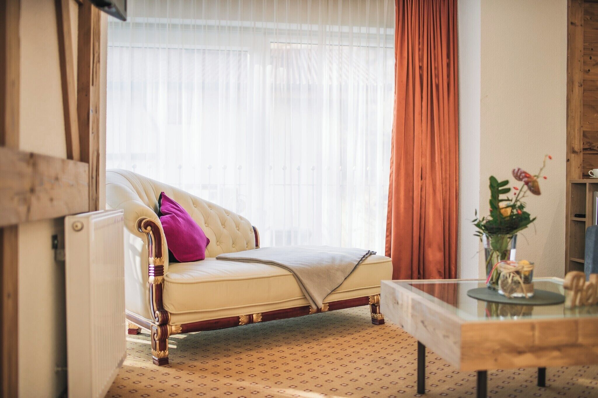 A room with a vintage sofa, a glass coffee table, and a window with curtains.