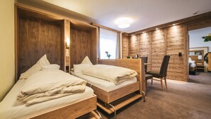 A hotel room with two wooden beds, a chair, and a wooden wall panel. - Arlen Lodge Hotel (Sankt Anton am Arlberg)