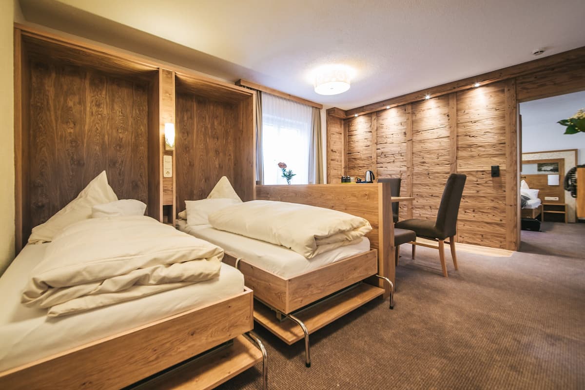 A hotel room with two wooden beds, a chair, and a wooden wall panel.