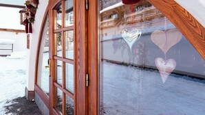 A wooden door with a glass panel, a reflection of a building, and a heart-shaped decoration on the wall. - Arlen Lodge Hotel (Sankt Anton am Arlberg)