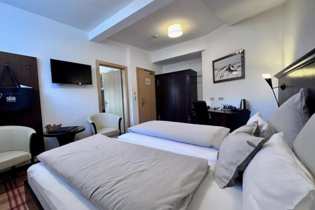 A hotel room with a bed, two chairs, a desk, a TV, and a wardrobe.