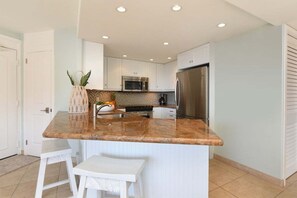 Een moderne keuken met witte kasten, een granieten aanrechtblad, roestvrijstalen apparatuur en een klein eiland met barstoelen.