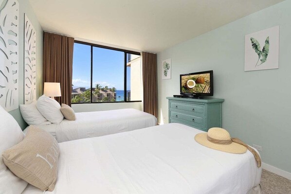 Een hotelkamer met twee bedden, een televisie op een dressoir en uitzicht op de oceaan.