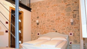 A bedroom with a stone wall, a bed with white linens, two bedside tables, and a wooden door. - B&B Tito Livio (Teolo)