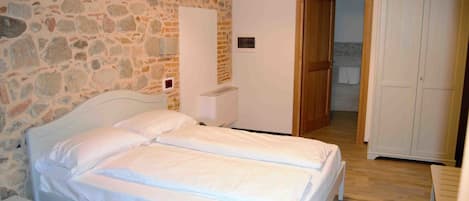 A bedroom with a stone wall, a wooden door, and a white wardrobe.