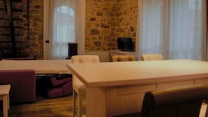 A room with a stone wall, a bed, a TV, and a dining table with chairs. - B&B Tito Livio (Teolo)