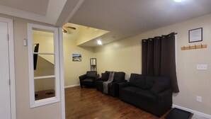 Un soggiorno con pavimento in legno, due divani neri, un tavolino, un quadro appeso al muro e una lampada a soffitto.