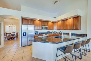 A modern kitchen with a central island, stainless steel appliances, wooden cabinets, and bar stools. - Chandler Lakefront Heated Pool • Golf, Sunsets (Chandler)