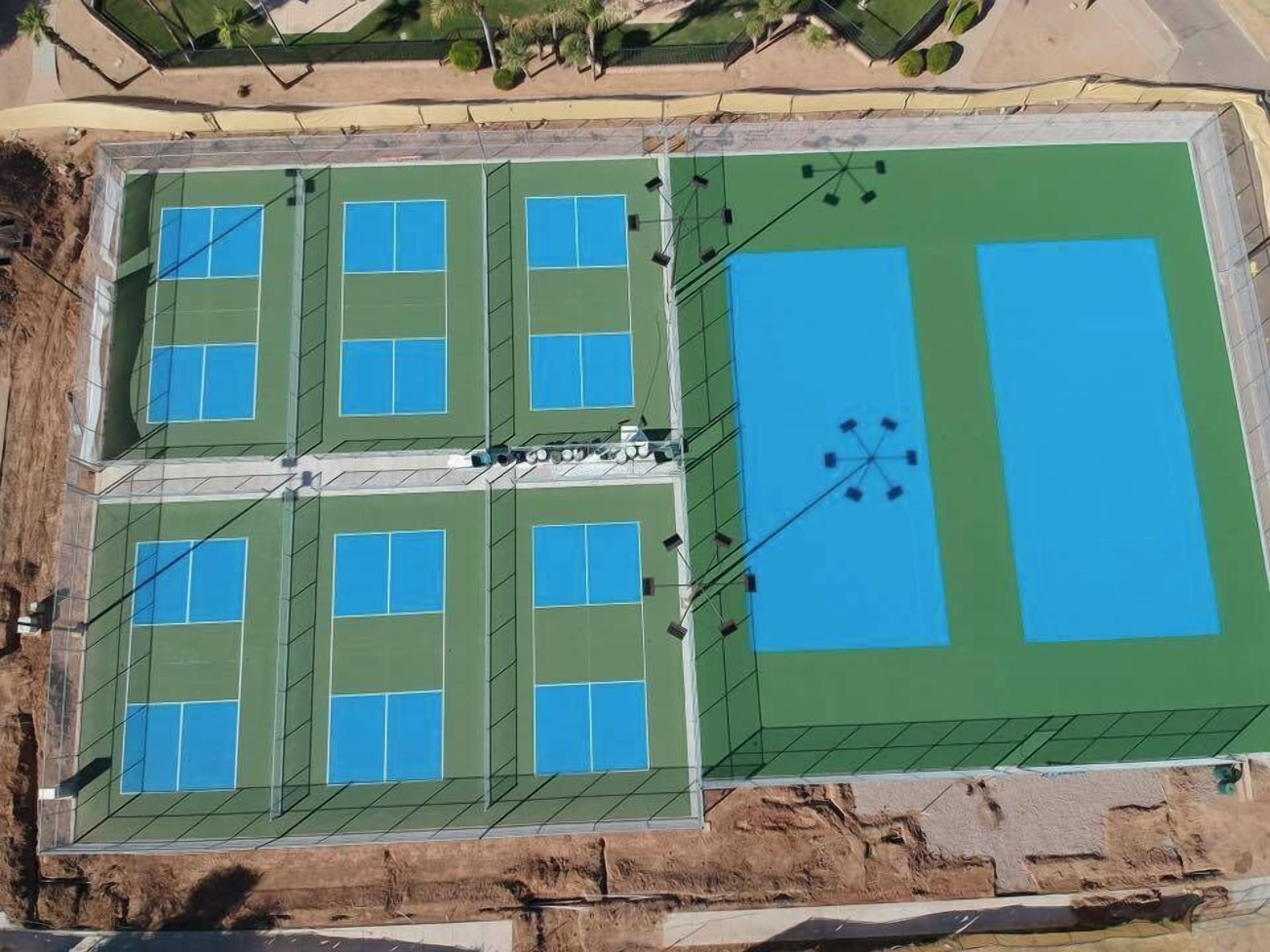 An aerial view of a sports facility with multiple tennis courts and a large green field.