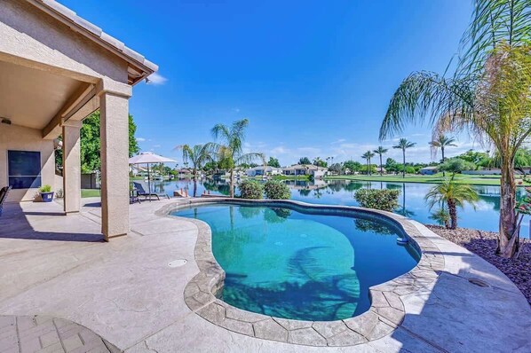 A swimming pool with a curved edge, surrounded by a stone deck and palm trees. - Chandler Lakefront Heated Pool • Golf, Sunsets (Chandler)