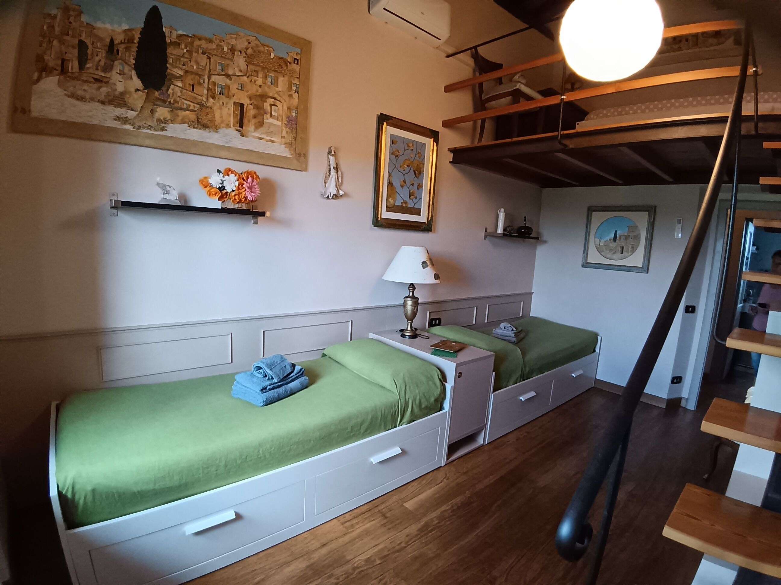 Une chambre avec deux lits simples, une table de chevet, une lampe, un tableau et un escalier.