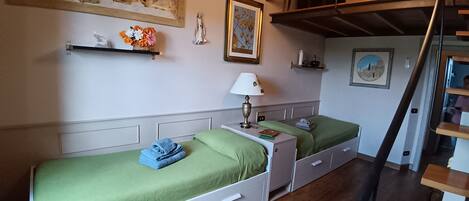 Une chambre avec deux lits simples, une table de chevet, une lampe, un tableau et un escalier.