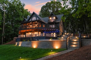A large, multi-story house with a porch, a staircase, and a well-lit exterior. - Huckleberry Hideout by SoCharm | Private Cabin Oasis (Mooresville)