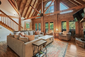 A spacious living room with a wooden ceiling, large windows, a sofa, a coffee table, and a fireplace. - Huckleberry Hideout by SoCharm | Private Cabin Oasis (Mooresville)