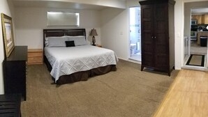 A bedroom with a bed, a nightstand, a lamp, a wardrobe, and a view of the kitchen through an open door. - Skiing, Mt Biking, Climbing, Hiking, Boating, Swimming, ATV Trails. (Bountiful)