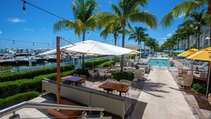 Un espace extérieur aménagé avec une terrasse, des sièges, une piscine et, au loin, un port de plaisance.