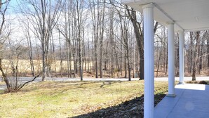 A covered outdoor area with white columns, surrounded by a wooded area.