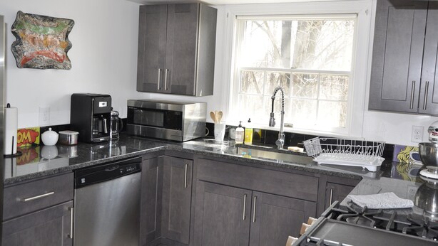 A modern kitchen with stainless steel appliances, dark cabinets, and a large window providing natural light.