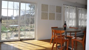 A dining area with a table and chairs, a bottle of wine, and a view of a garden through a large window.