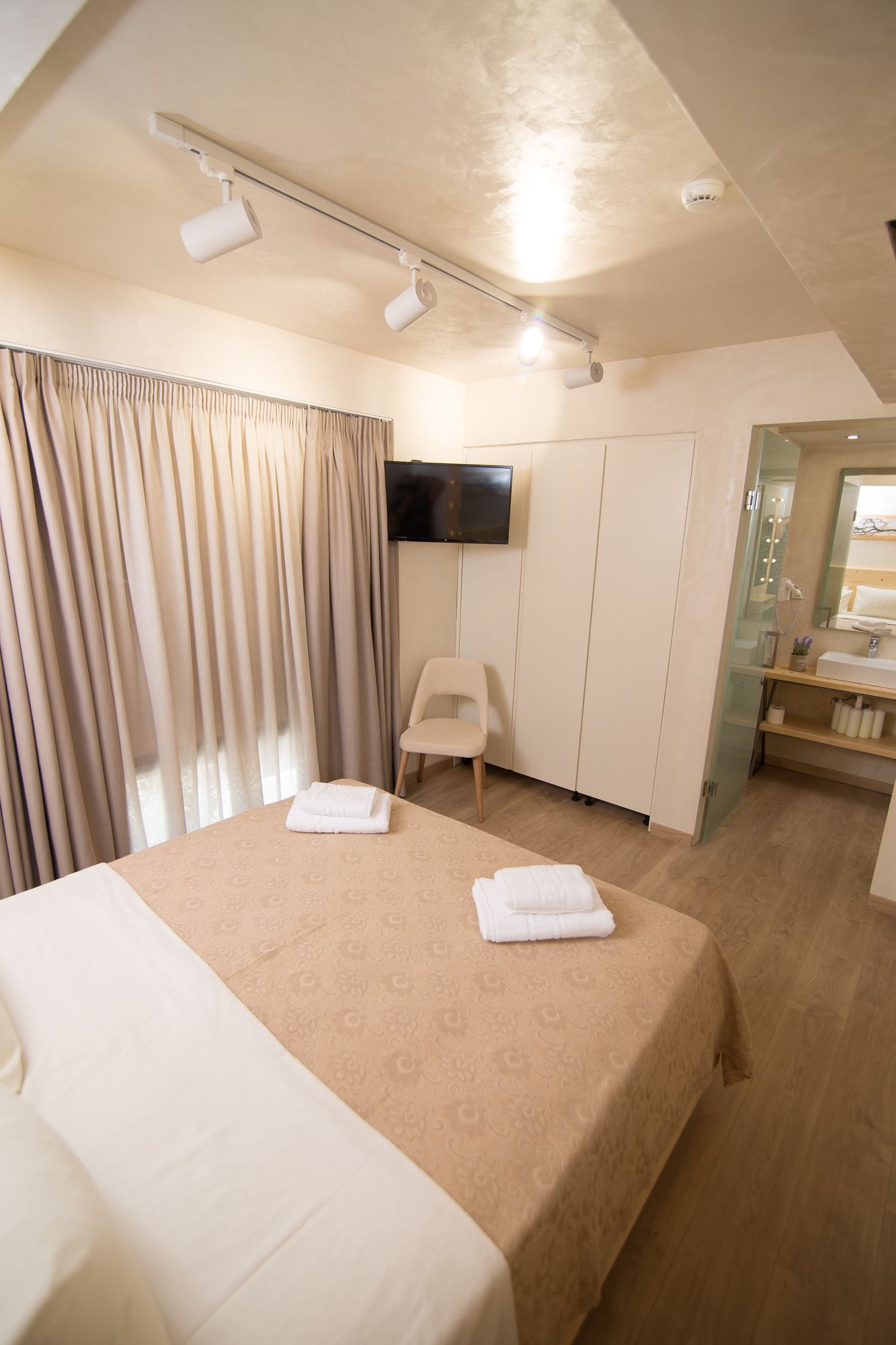 A hotel room with a large bed, a television, a chair, and a bathroom with a mirror and sink.
