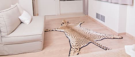 A room with a wooden ceiling, a sofa, a leopard print rug, and a window with curtains.