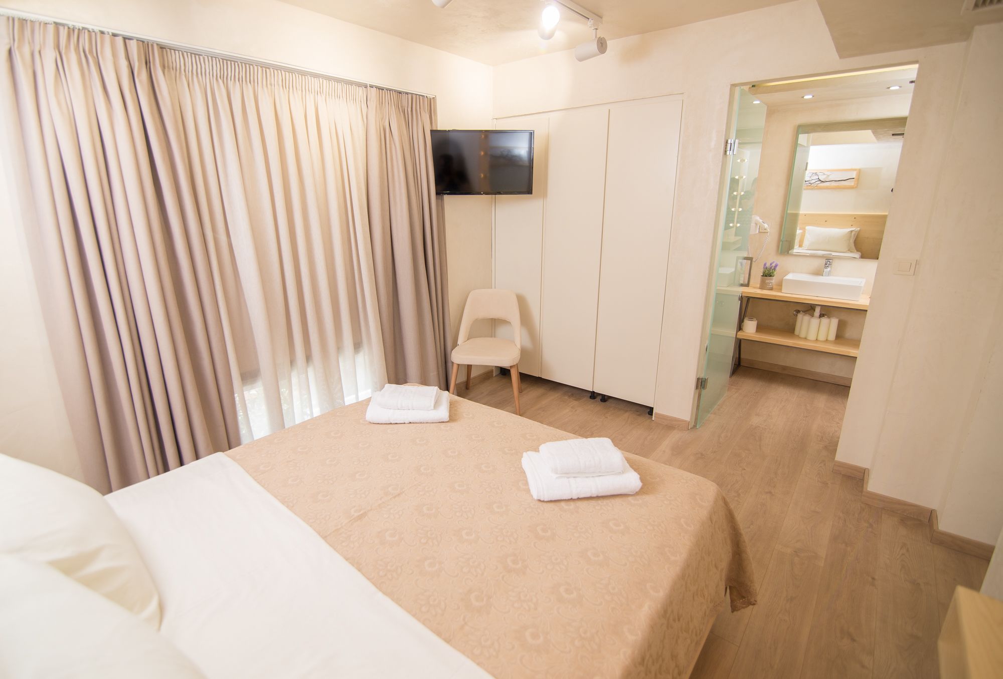 A hotel room with a bed, a TV, a chair, and a bathroom visible through an open door.
