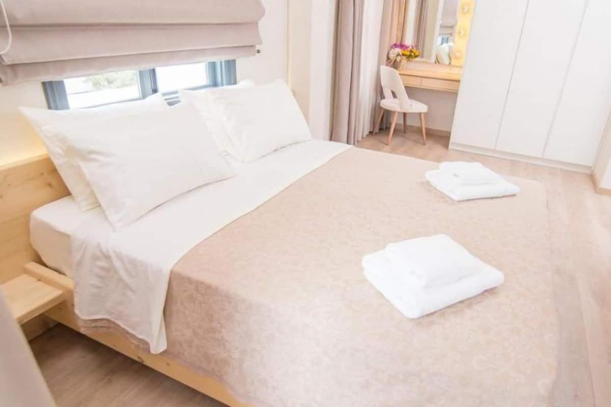A neatly made bed with white linens, a wooden headboard, and a window with curtains.