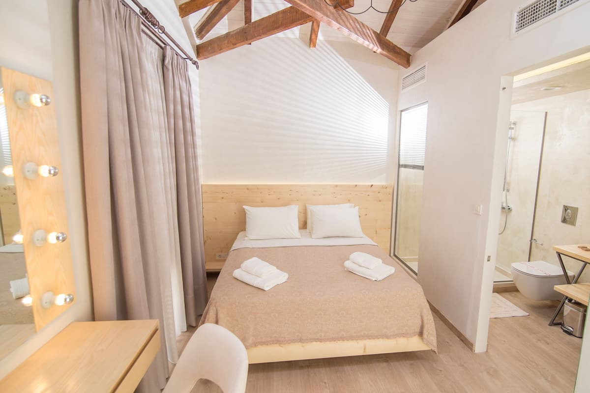 A hotel room with a wooden headboard, a large mirror with lights, a bed with white linens, and a wooden desk.