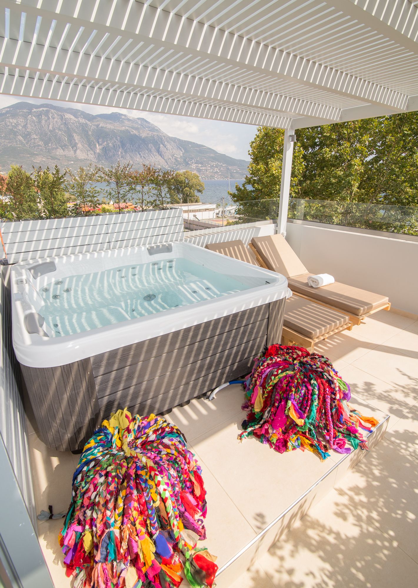 Un jacuzzi con vistas a las montañas, una pila de toallas coloridas y sillones de descanso en una terraza.