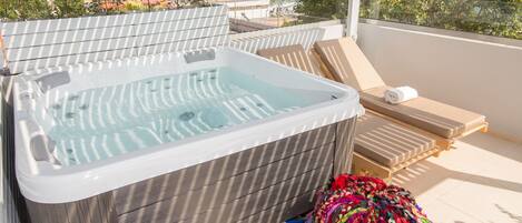 Un jacuzzi con vistas a las montañas, una pila de toallas coloridas y sillones de descanso en una terraza.