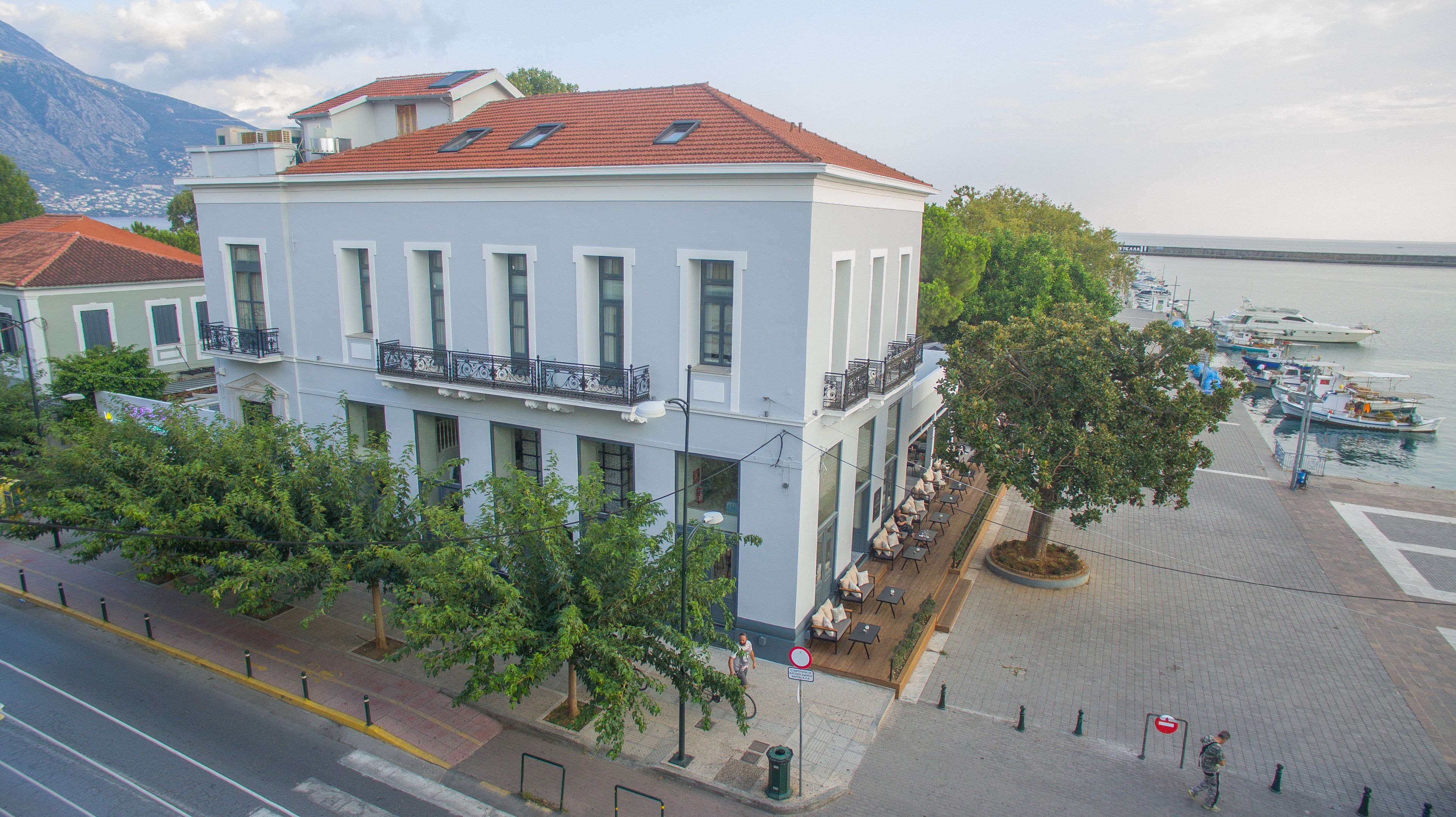 Un edificio de dos plantas con un balcón, una zona ribereña pavimentada y vistas a barcos.