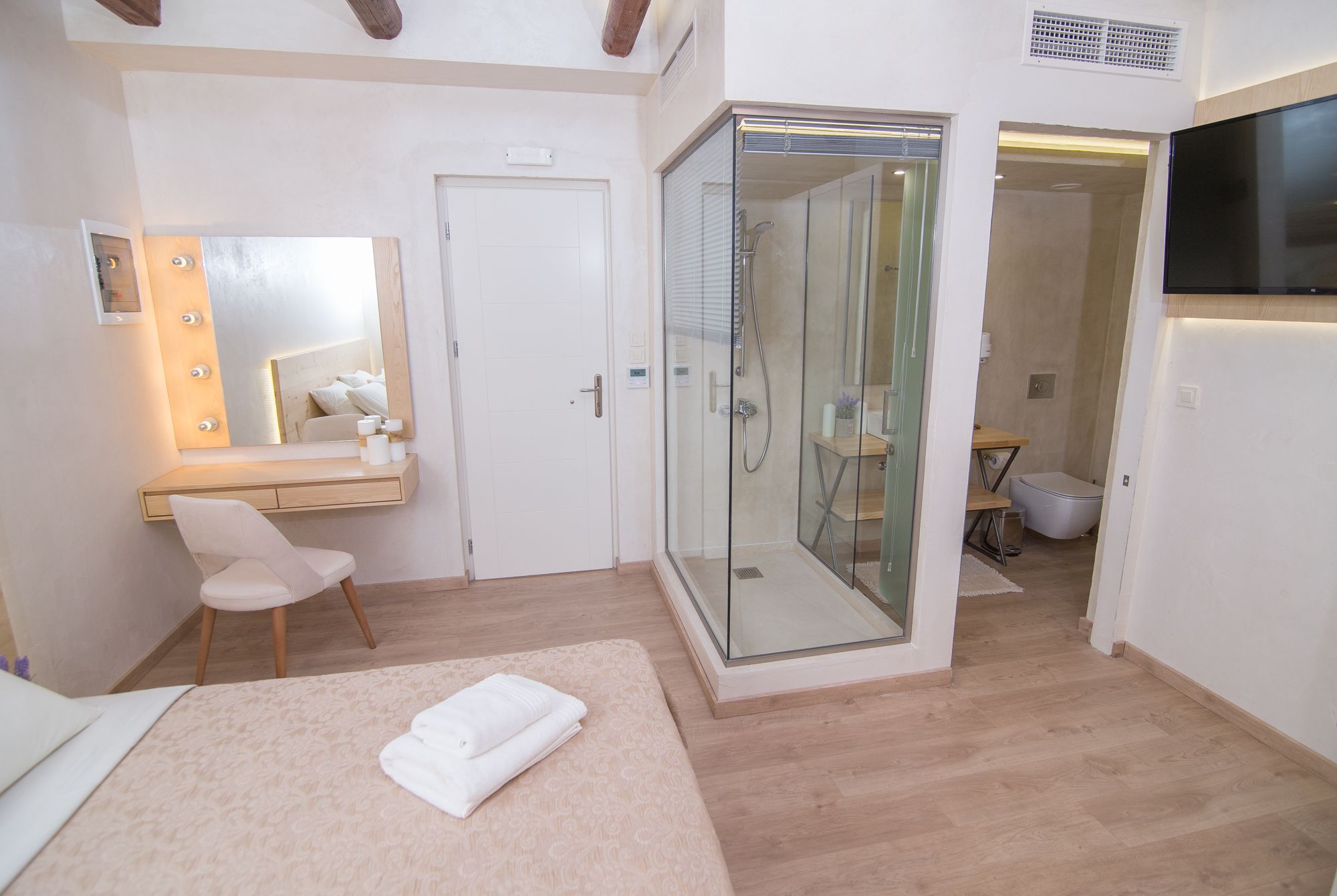 A bedroom with a bed, a vanity with a mirror, a shower enclosure, and a television.